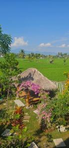 a grass hut with purple flowers in a field at Mantra Yoga Homestay in Tanjung