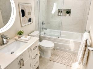 a white bathroom with a tub and a toilet and a sink at Walk Everywhere from This Bright 2BR Condo in Vancouver