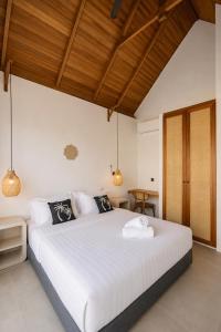 a bedroom with a large white bed with wooden ceilings at FinnKai Villas in Sengkol
