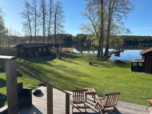 a deck with two chairs and a table and a lake at Sjötomt med bastuflotte & badtunna - lantlig idyll in Vingåker