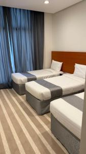 three beds in a room with blue curtains at فندق العلاء 4 in Al Masfalah