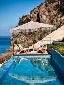 a swimming pool with chairs and an umbrella and the ocean at The Cliff Residences in Plomari