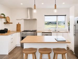 a kitchen with white cabinets and a wooden island with stools at The Burnby in Te Anau