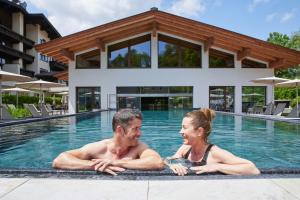 a man and a woman laying in a swimming pool at Das Walchsee Resort in Walchsee
