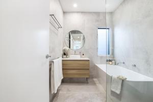 a bathroom with a tub and a sink and a mirror at Basalt Beach House in Bargara +32 photos