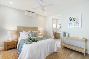 a white bedroom with a bed and a ceiling fan at Basalt Beach House in Bargara