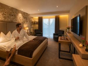 a man sitting on a bed in a hotel room at Kurhotel Grüttner mit eigenem Sole Thermal Schwimmbad 32 Grad und Saunalandschaft in Erwitte