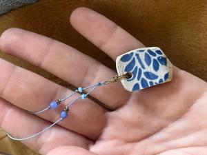 a hand holding a necklace with a blue and white stone at Clinica apartments in Bologna +2 photos
