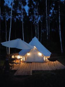 a white tent with a table and umbrellas at night at Glempings Pasaka un pirts I tent and sauna in Vecumnieki +9 photos