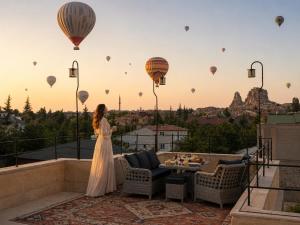 a woman in a white dress standing on a balcony with hot air balloons at Üçhisar Palace İn Cappadocia in Uçhisar