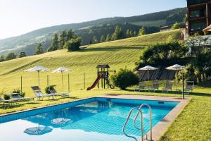 a swimming pool with a playground and a hill at Hotel Tyrol in Funes