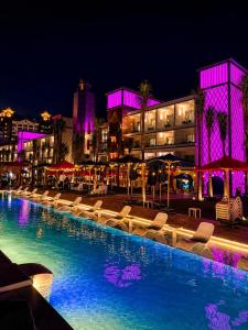 a swimming pool with chairs and buildings at night at M Hotels at Porto Marina in El Alamein