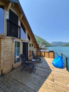 a wooden deck with chairs and a house on the water at Splav Zaliv, Perućac in Aluga