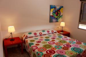 a bedroom with a bed with a colorful bedspread and two lamps at Apartamentos Guillem in Playa de Miramar