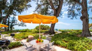 a table and chairs under an umbrella with the beach in the background at Bamboo Apartments in Holmes Beach