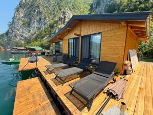 a wooden deck with chairs and a house on the water at Splav Astra Perućac in Perućac