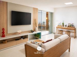 a living room with a couch and a tv on a wall at Casa Ilha do Sol - Vera Cruz/BA in Vera Cruz de Itaparica