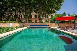 a swimming pool with chairs and a red umbrella at 5 Family Apartments with Pool & Large Garden in Historic Pézenas Convent in Pézenas