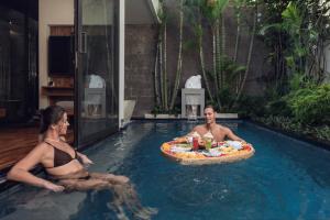 a man and woman sitting in a swimming pool with a pizza at Ayona Villa Seminyak by Ini Vie Hospitality in Seminyak