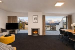 a living room with a fireplace and a table and a television at Alpine Vista with Mountain Views, Pool and Spa in Wanaka
