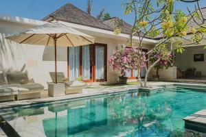 a swimming pool with an umbrella and a house at Jivana Resort in Kuta Lombok