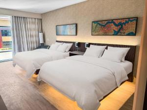 two beds in a hotel room with white sheets at Cambria Hotel Jacksonville in Jacksonville