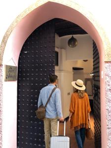 a man and woman walking through an arch with luggage at Riad ABBASSIA Marrakech Première - Authentic Medina Experience in Marrakesh