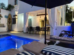 a swimming pool with an umbrella next to a house at Villa Alhamar con piscina climatizada privada in Punta Umbría