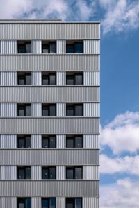 a tall grey building with a cloudy sky in the background at Hôtel Les Loges in Geneva