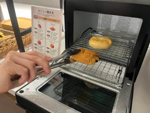 a person holding a spatula cooking a bagel in an oven at plat hostel keikyu minowa forest in Tokyo