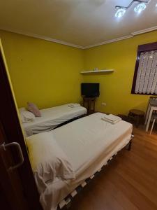 two beds in a room with yellow walls at Hostal Inés in Boñar