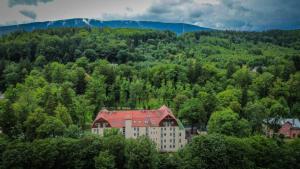a building with a red roof in the middle of a forest at Hotel Nowy Dwór Elizy blisko Sky Bridge in Długopole-Zdrój