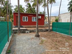 a red house with palm trees and a fence at Coco Kudil - FARM STAY in Salem