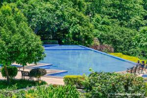 a large blue swimming pool in a garden with trees at Aloha Serenity By Evara -Ganga View Stays in Rishīkesh