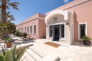 a pink building with a courtyard and palm trees at Rose Bay Hotel in Kamari