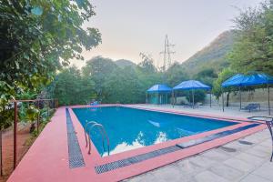 a swimming pool with two blue umbrellas at Sariska Forest Trail in Rāmsinghpura +58 photos