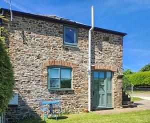 a stone house with two windows and a blue table outside at Three Little Pigs in Bude