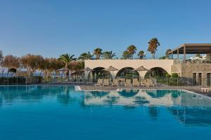 a large swimming pool with chairs and a building at Atlantica Beach Resort Kos in Kardamaina