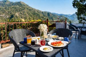 a table with plates of food on a balcony with mountains at Kumaon Cottage, Nainital - AM Hotel Kollection in Nainital
