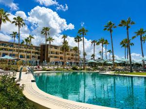 a swimming pool in front of a resort with palm trees at Hotel Punta Bermeja Premium in El Puerto de Santa María