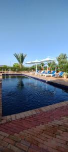 a swimming pool next to a beach with lounge chairs at Les Plamiers d'anis in Ouarzazate