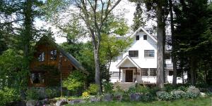 a white house with trees and flowers in front of it at Kamishiro Mountain Lodge in Hakuba