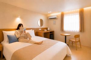 a woman sitting on a bed reading a book at 부산 수영 블루닷 호텔 in Busan