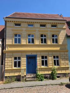 a yellow house with a blue door on a street at Apartment 2 im Martinsgarten Angermünde in Angermünde