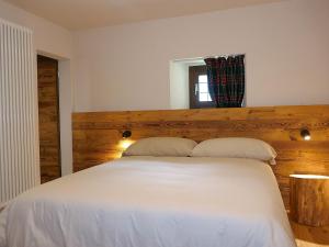 a bedroom with a white bed with a wooden headboard at Apartment Rina by Interhome in Olivone