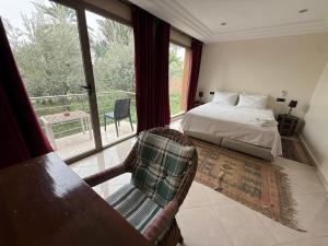 a bedroom with a bed and a chair and a window at Les Plamiers d'anis in Ouarzazate