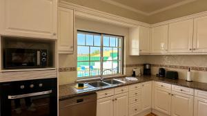 eine Küche mit weißen Schränken, einer Spüle und einem Fenster in der Unterkunft Abby - Private Pool - 11 Guests - Albufeira in Albufeira