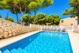 a swimming pool with chairs and a stone wall at Villa Trepuco Dos in Punta Prima