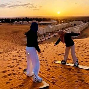 two children are playing on surfboards in the sand at Sahara Starlight camp in Merzouga