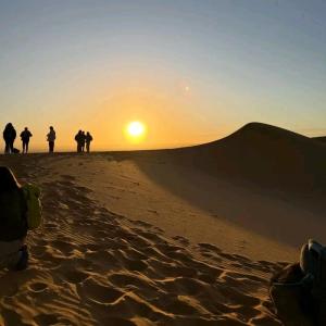 a group of people walking in the desert at sunset at Sahara Starlight camp in Merzouga